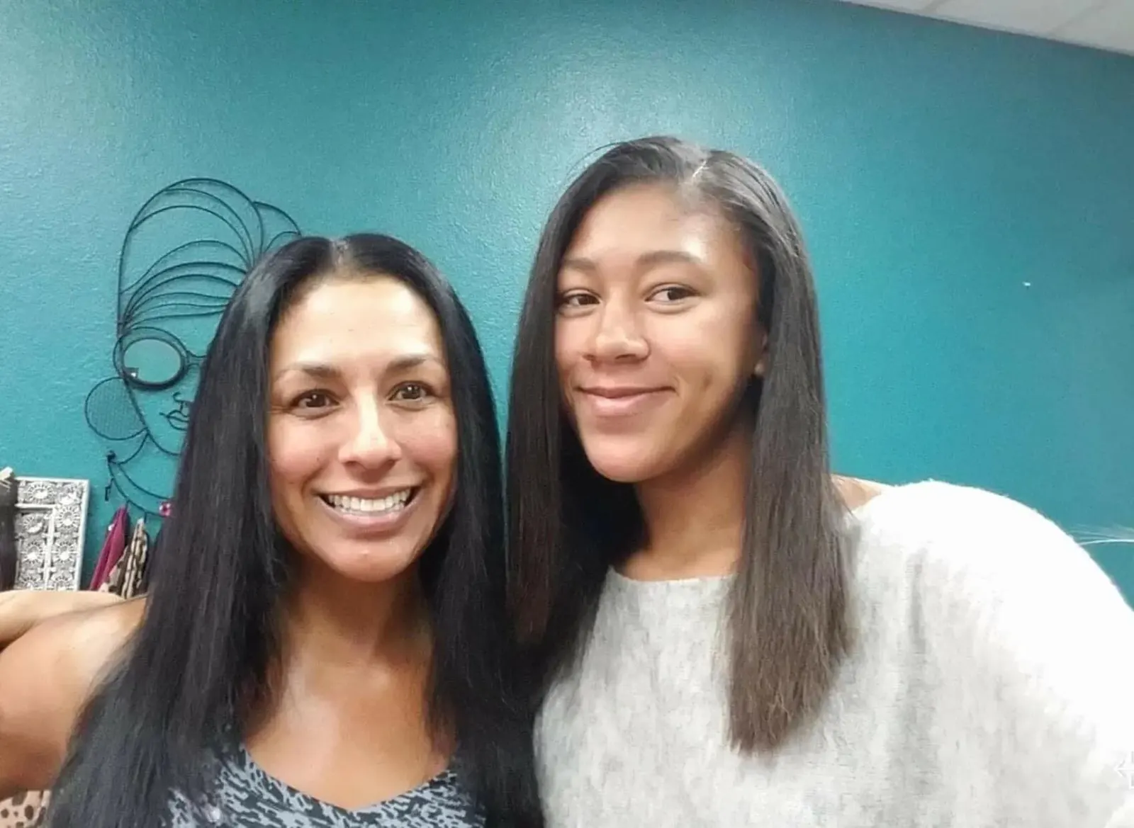 Mother and daughter smiling with long dark hair against teal wall